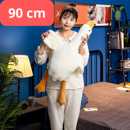 Person holding a large white plush toy with yellow feet in a room with a blue wall and furniture. 90cm goose