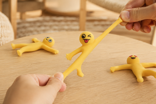 Yellow Stretchy Buddies™ sensory toy being stretched by hand on wooden table for stress relief and screen-free play