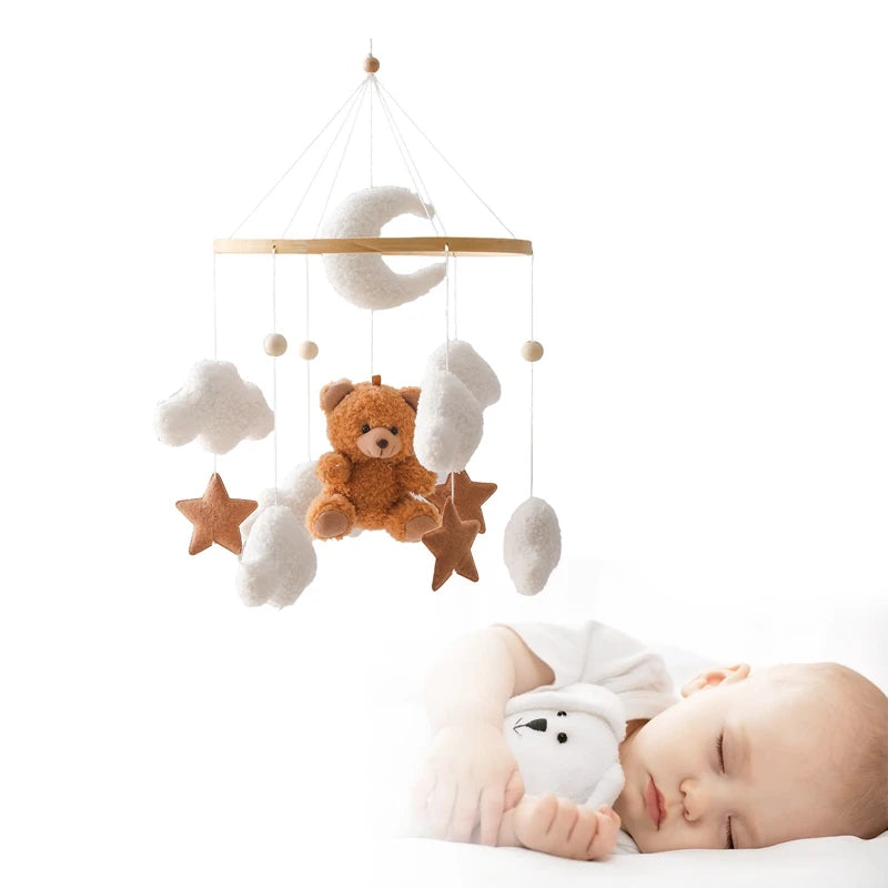 Baby sleeping with a crib mobile featuring teddy bear, stars, and clouds on a white background