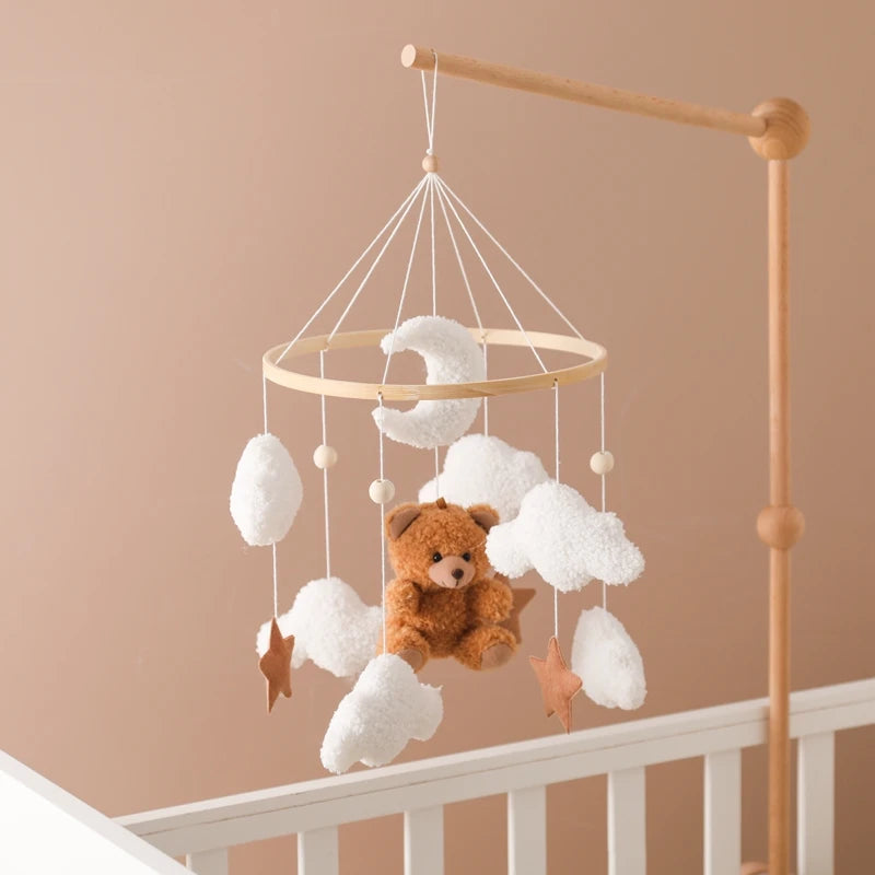 Baby mobile with teddy bear and clouds hanging above a crib against a beige wall.