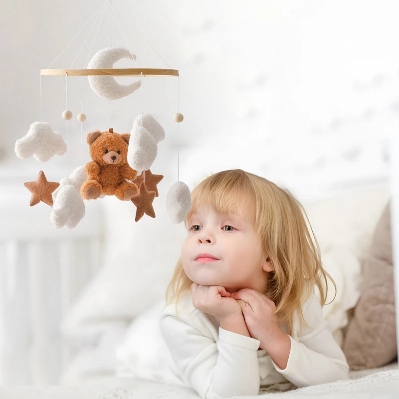 Child lying in bed with a teddy bear and cloud mobile above