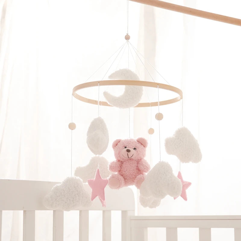 Baby crib mobile with pink teddy bear, clouds, and stars hanging above a crib.