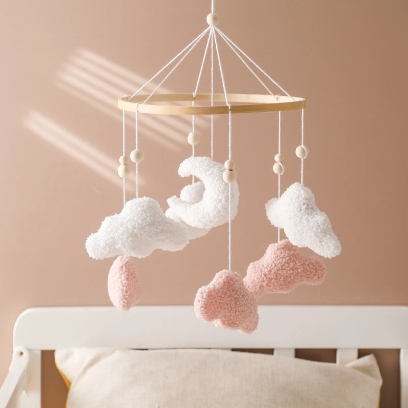 Decorative cloud mobile hanging above a crib with a soft pink wall background