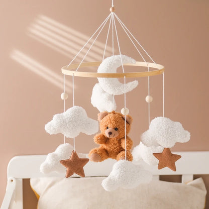 Baby mobile with teddy bear, clouds, and stars hanging above a crib against a beige wall.