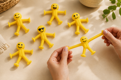 Yellow bendy man toys with smiling faces on a light surface, one being held by a hand.