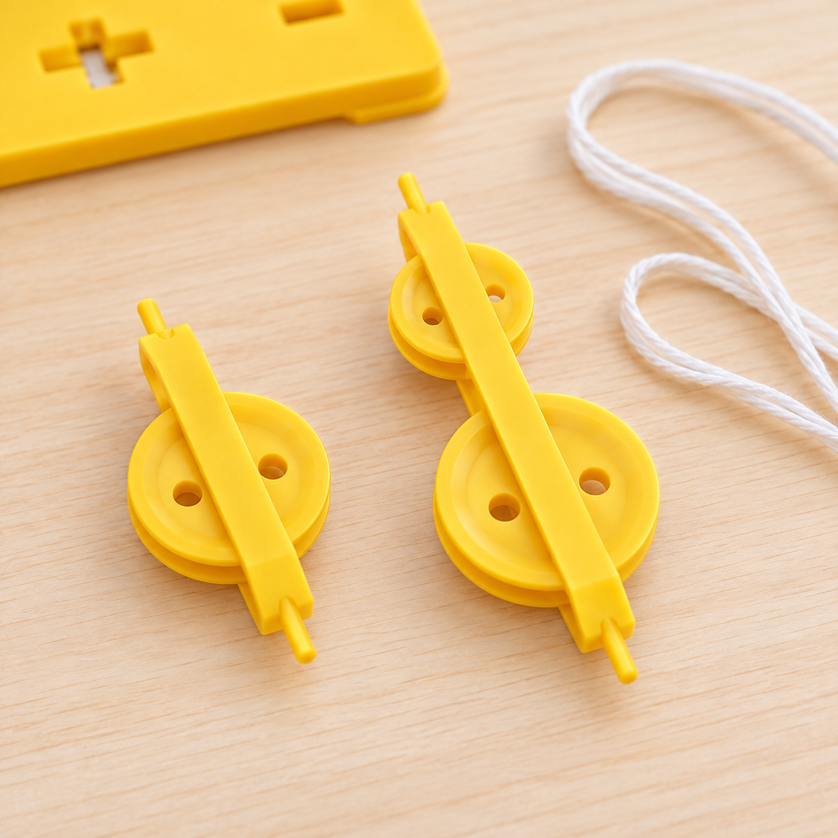 Close-up of yellow single and double pulley units on a wooden table, with white cord alongside and part of the support base in the background.