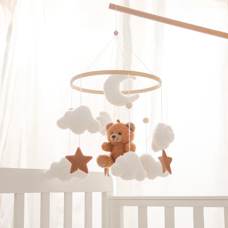 Baby crib mobile with teddy bear, stars, and clouds against a white curtain background