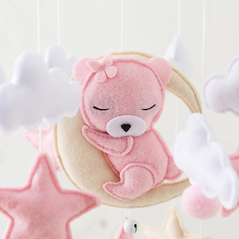 Pink teddy bear plush toy hanging from a cloud-themed crib mobile.