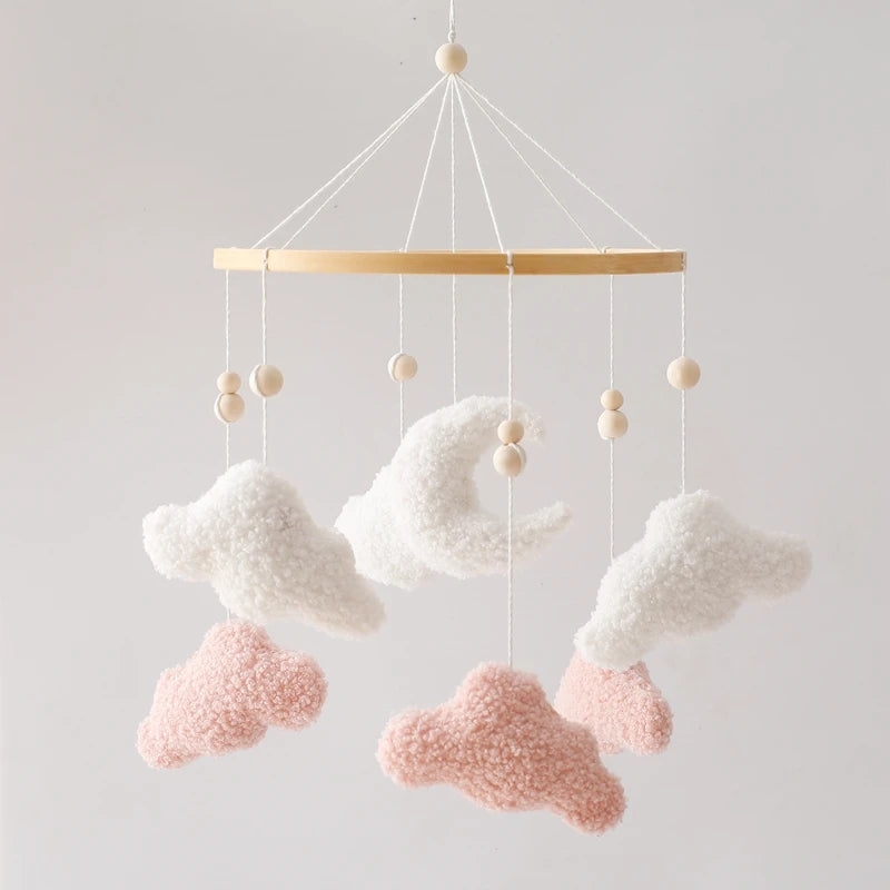 Decorative cloud mobile with pink and white clouds hanging from a wooden bar against a light gray background.