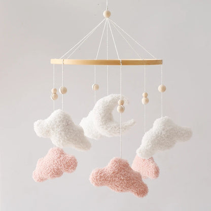 Decorative cloud mobile with pink and white clouds hanging from a wooden bar against a light gray background.