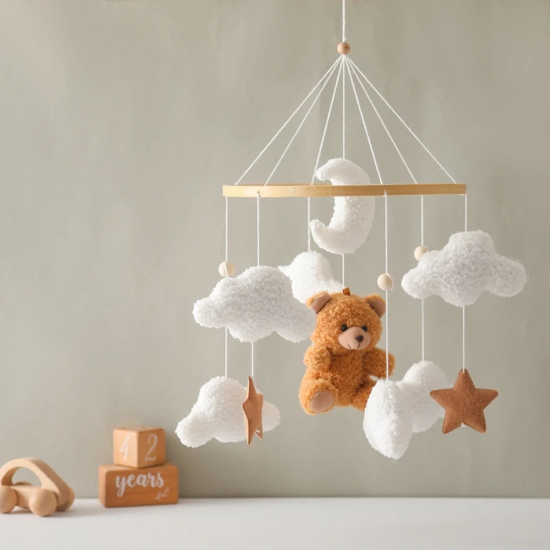 Children's mobile with teddy bear and clouds hanging against a neutral wall.