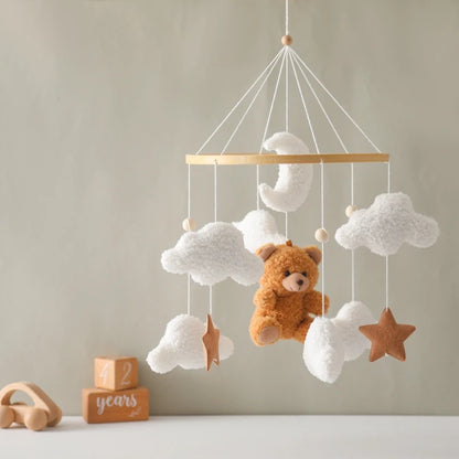 Children's mobile with teddy bear and clouds hanging against a neutral wall.